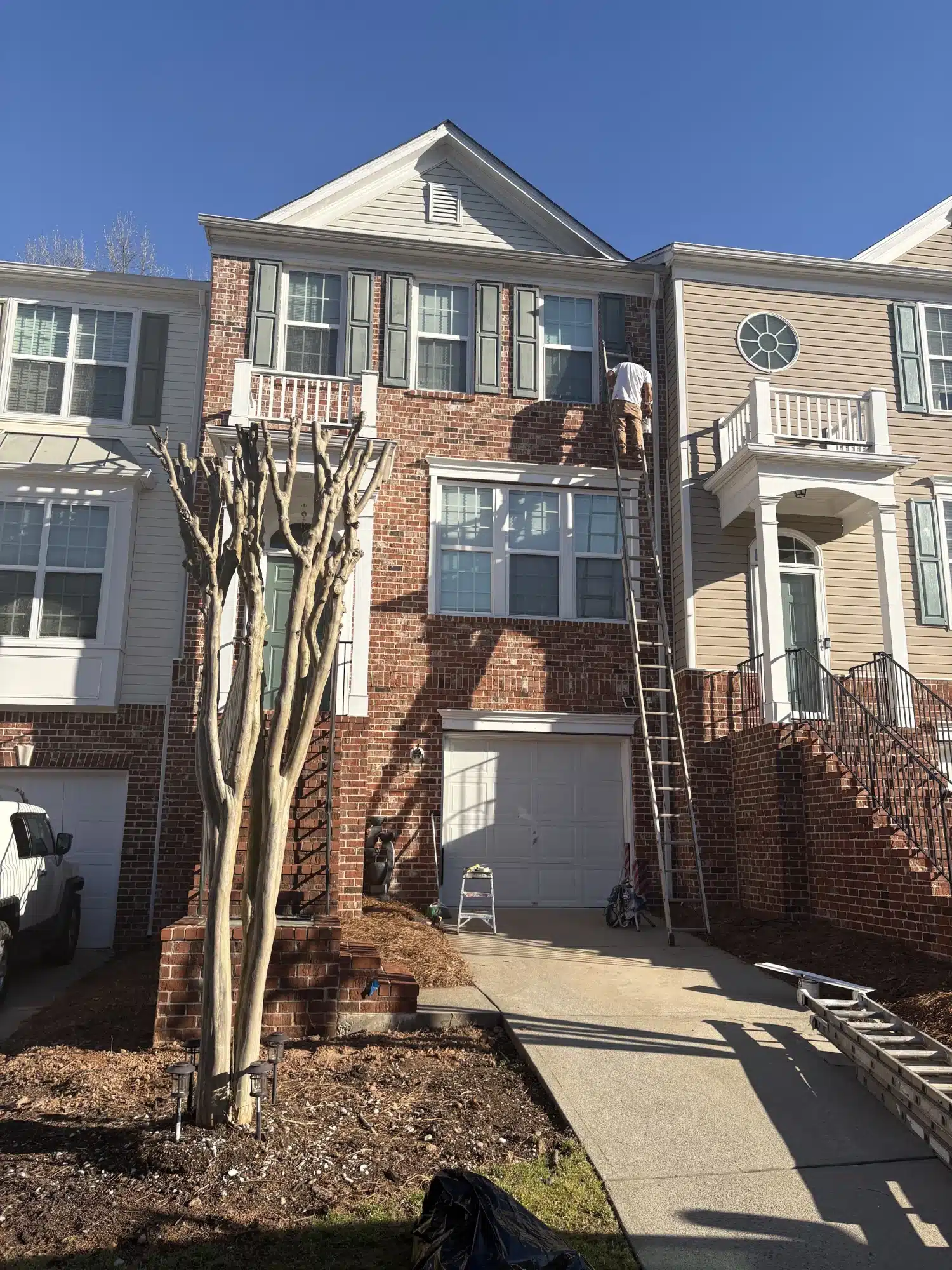 Brick townhome exterior with ladder during trim painting — MG Barillas Painting