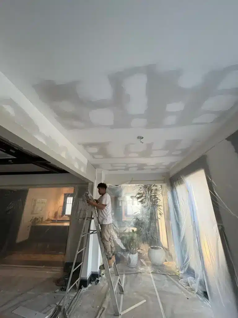 Painter on a ladder patching ceiling drywall before paint — MG Barillas Painting