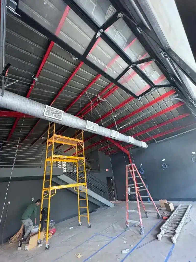 Commercial interior with red steel beams and charcoal walls mid-project — MG Barillas Painting