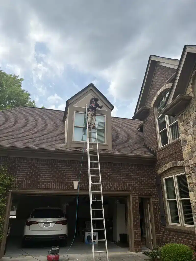 Painter on a ladder at a brick home gable — MG Barillas Painting